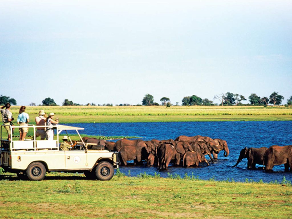 Tourists in a safari jeep watching elephant drink , shower. at Etosha National Park Namibia